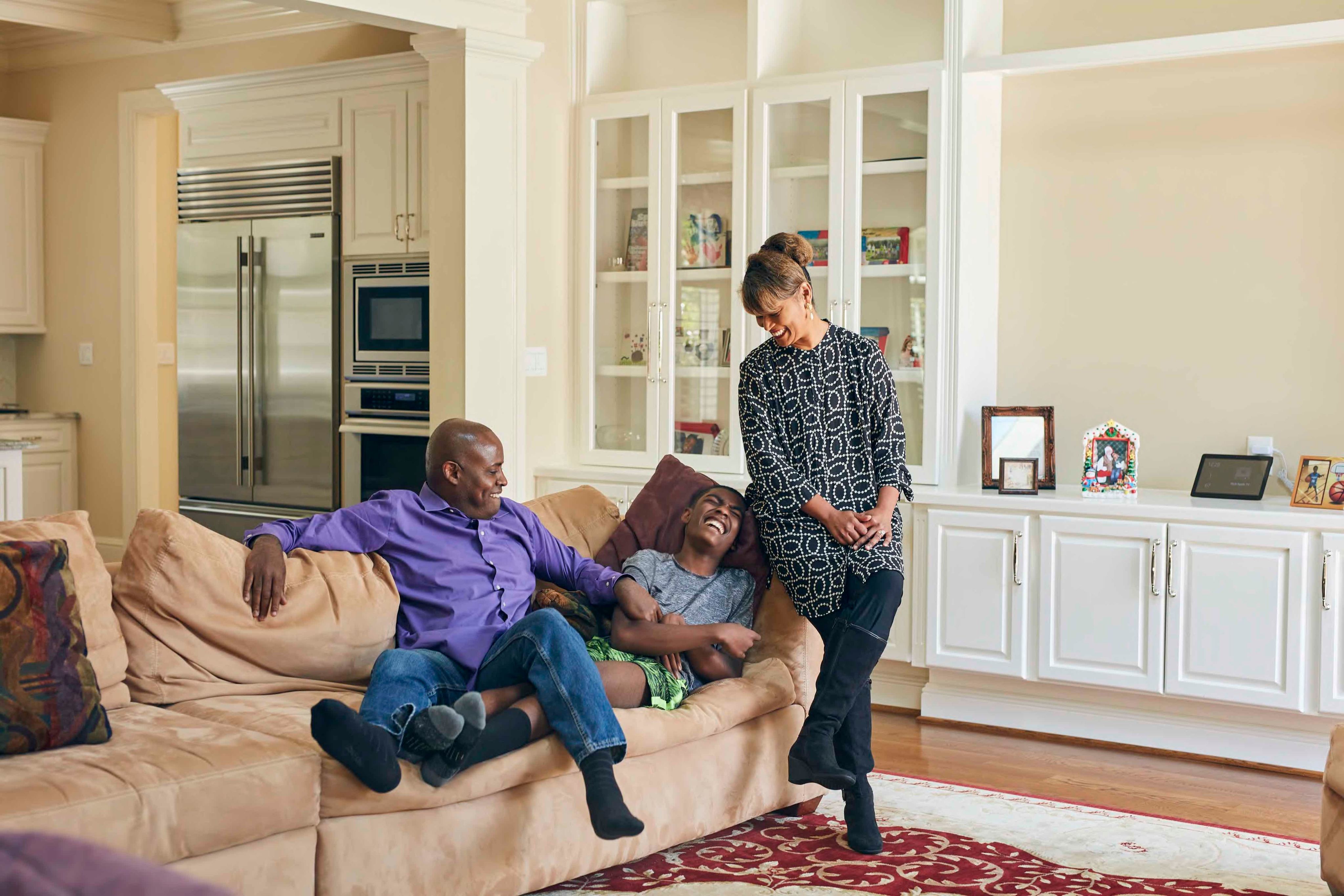 Parents and their teenage son laughing while sitting on a couch